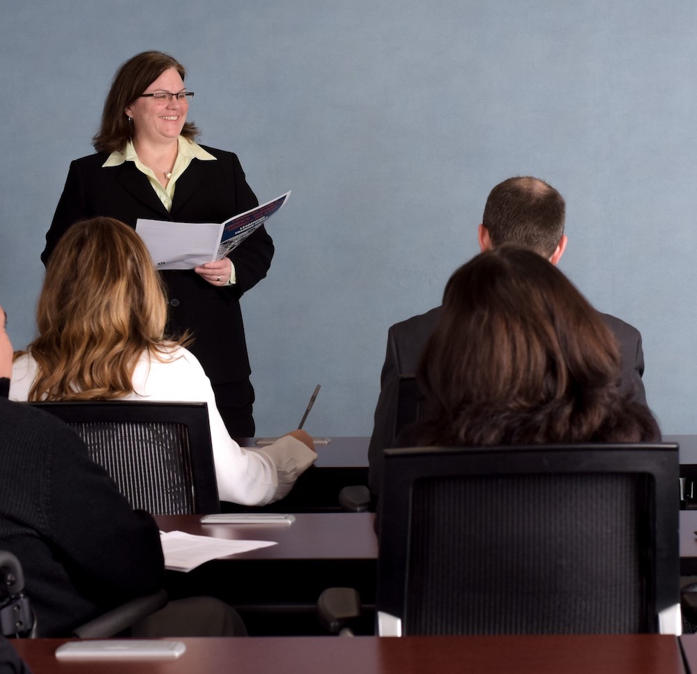 Person presenting in front of a classroom. everyone is wearing suits