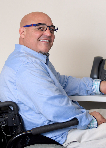 man employee in a wheelchair that is pointed away from camera, has his head turned to the camera and is smiling